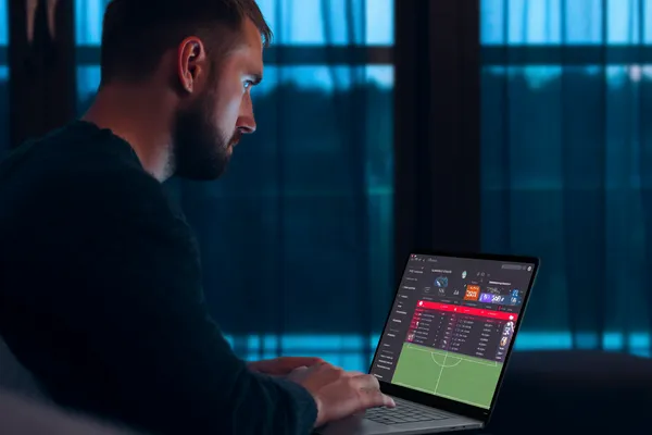 UUOK মোবাইল অ্যাপ — ক্যাসিনো ও স্পোর্টসের সম্পূর্ণ হাব একজন পুরুষ তার ল্যাপটপে মনোযোগ দিয়ে কাজ করছেন, ব্যাকগ্রাউন্ডে লাইভ স্ট্যাটস — যা UUOK মোবাইল অ্যাপের স্পোর্টস ও গেমিং ফিচারগুলোকে তুলে ধরে।